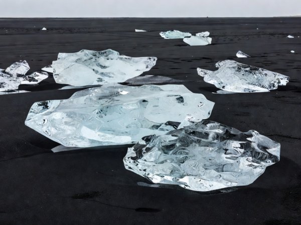 Documentary photograph of translucent glacial ice blocks resting on dark volcanic sand at Breiðamerkursandur, Iceland