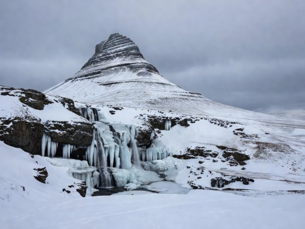 Documentary photograph of Kirkjufell mountain and partially frozen waterfalls on the Snæfellsnes Peninsula, West Iceland